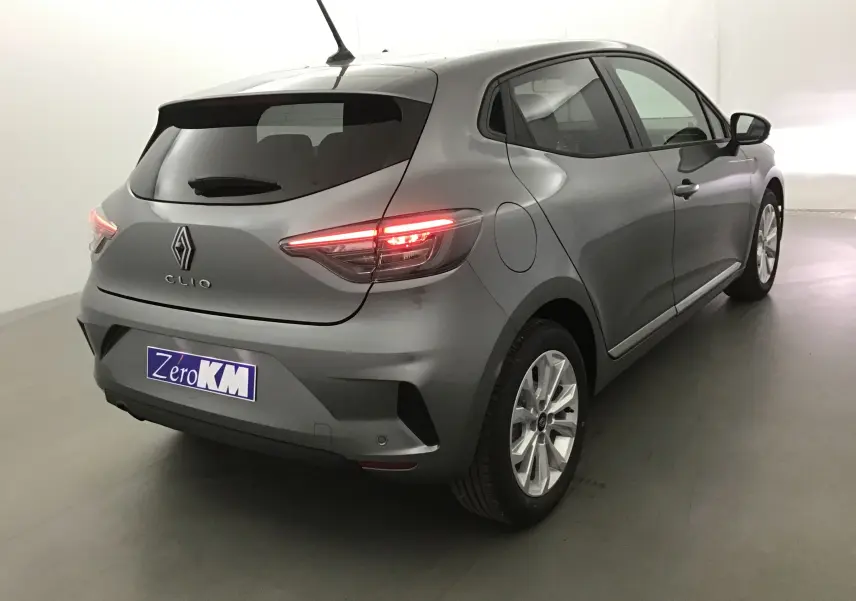 Vue 3/4 arrière droite d'une Renault Clio V gris schiste avec feux allumés et protections latérales chromées visibles.