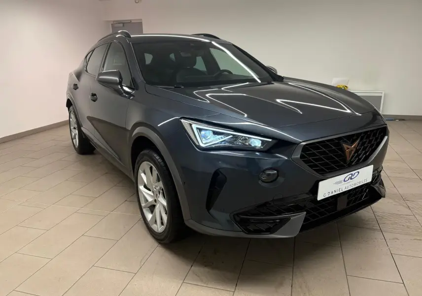 Vue 3/4 avant du CUPRA Formentor 1.5 TSI 150 DSG7 en gris magnétique, avec calandre noire et phares LED allumés.