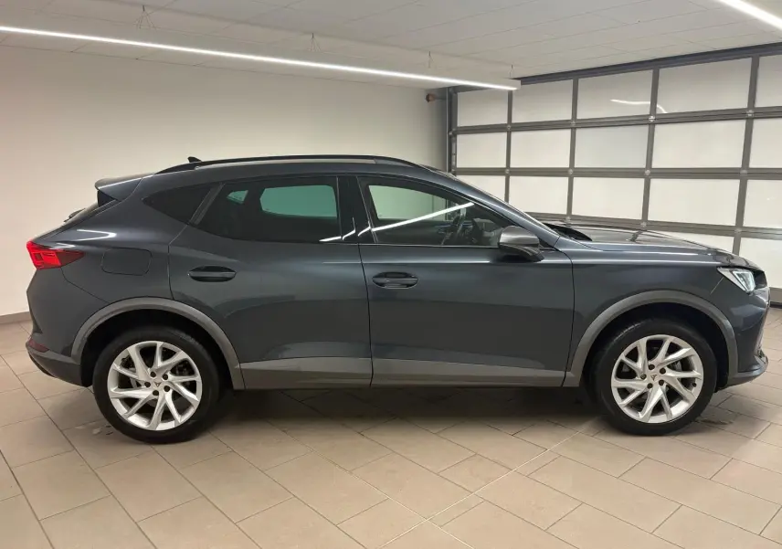 Vue de profil côté gauche d'un CUPRA Formentor 2024 gris magnétique avec jantes argentées en intérieur fermé.