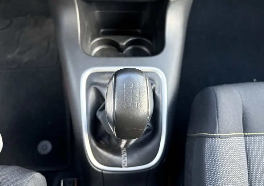 Le levier de vitesses manuel noir de la Citroën C3 rouge, vu de dessus au centre de l'habitacle.