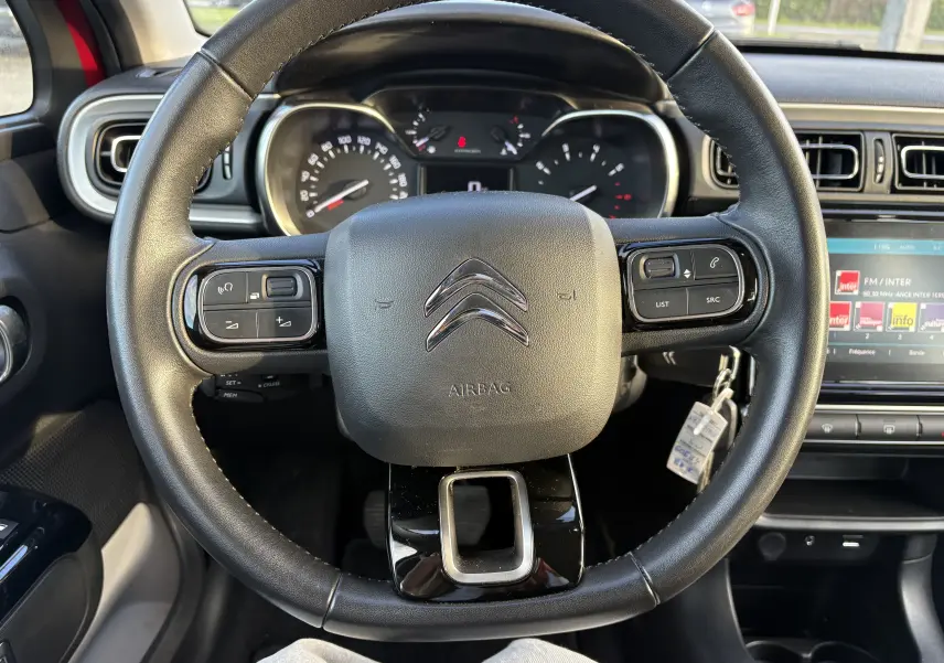 Vue intérieure centrée sur le volant noir de la Citroën C3 rouge, avec tableau de bord et écran multimédia visibles.