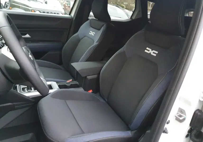 Vue intérieure côté conducteur du Dacia Duster blanc glacier 2025, sièges noirs avec logo distinctif brodé.