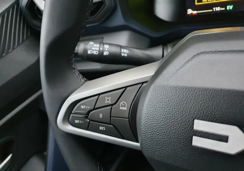 Gros plan sur les commandes au volant côté gauche du Dacia Duster blanc Glacier, affichage numérique en arrière-plan.