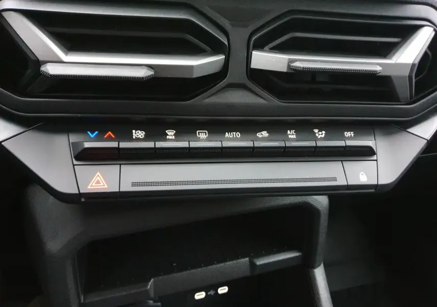 Vue rapprochée du tableau de bord du Dacia Duster blanc glacier 2025, montrant les commandes de climatisation et deux prises USB type C.