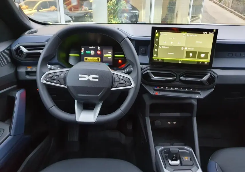 Vue intérieure frontale du tableau de bord du Dacia Duster blanc glacier, avec écran tactile et volant multifonction.