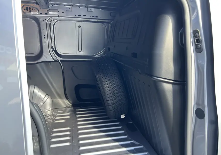 Intérieur de la zone de chargement côté droit du DANGEL Partner gris Artense avec une roue de secours appuyée contre la paroi.