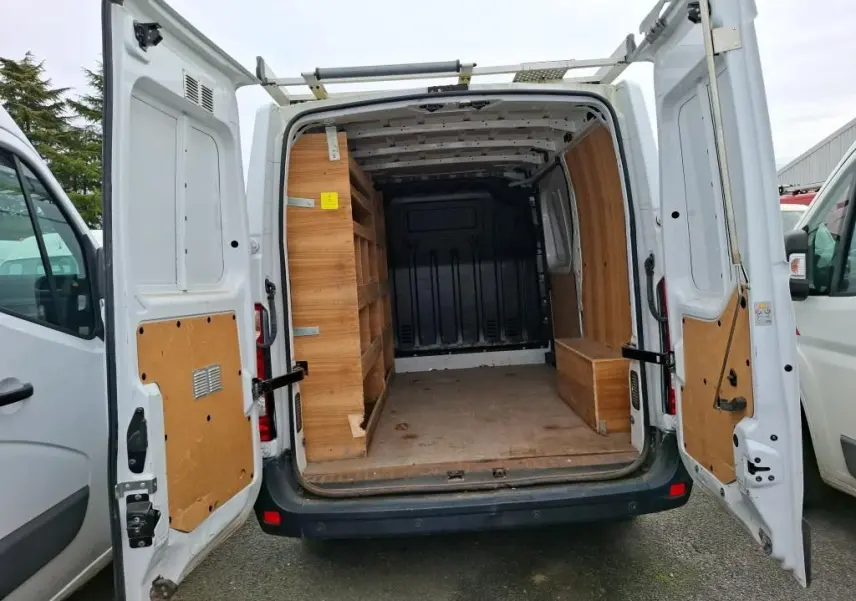 Vue arrière d’un Renault Master blanc 2019 avec portes ouvertes, montrant l’intérieur utilitaire équipé de rangements en bois.