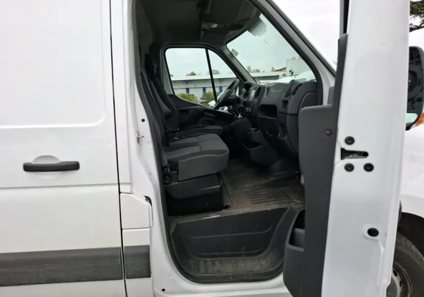 Vue latérale côté gauche du Renault Master blanc 2019 avec porte avant ouverte montrant l'intérieur cabine et les sièges noirs.