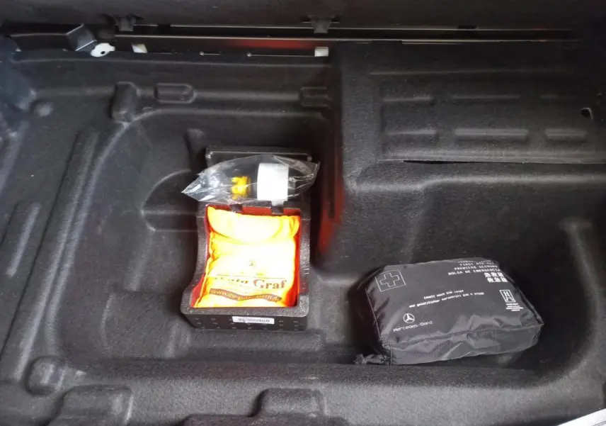 Coffre ouvert d’une Mercedes Classe C Coupé blanc, vue plongeante sur rangement avec trousse de secours et kit de réparation.