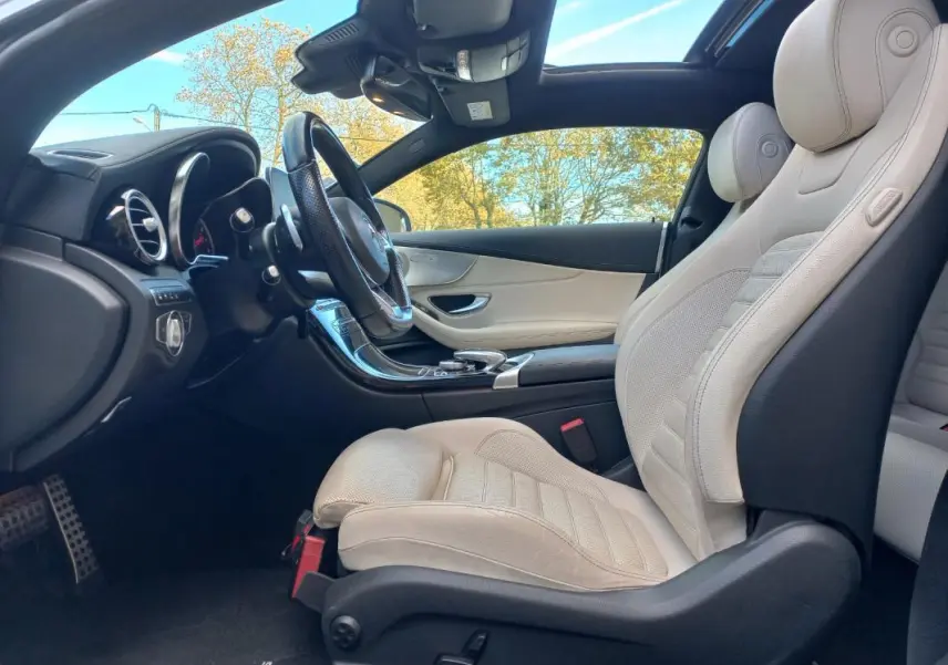 Vue intérieure côté conducteur de la Mercedes Classe C Coupé blanc avec sièges cuir beige et toit ouvrant panoramique.