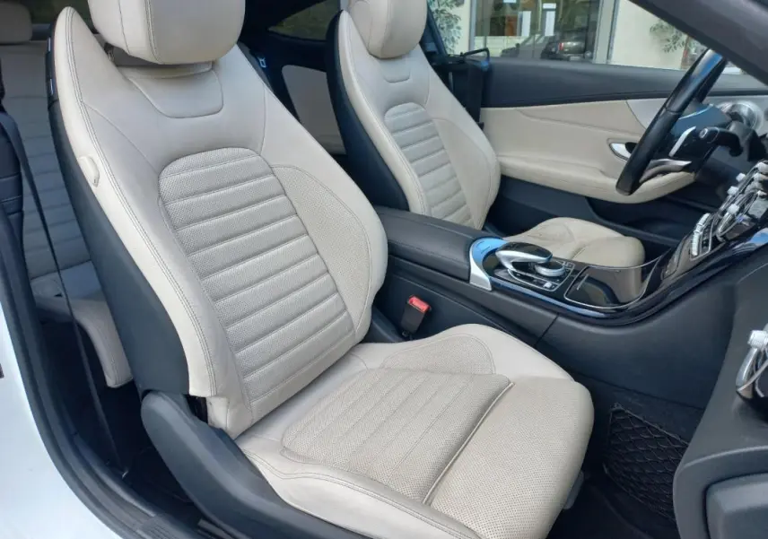 Vue intérieure côté conducteur montrant les sièges en cuir beige et la console centrale noire brillante d'une Mercedes Classe C Coupé blanche.