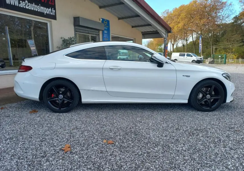 Vue de profil côté gauche d'une Mercedes Classe C Coupé blanc avec jantes noires et toit ouvrant électrique.