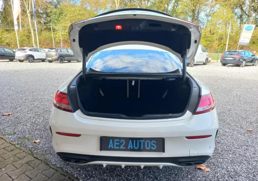 Vue arrière d'une Mercedes Classe C Coupé blanche 2016 avec coffre ouvert sur un parking extérieur.