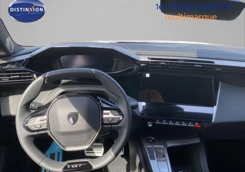 Vue intérieure centrée sur le volant GT et la console digitale d'une Peugeot 308 Hybrid blanche, finition 2026.