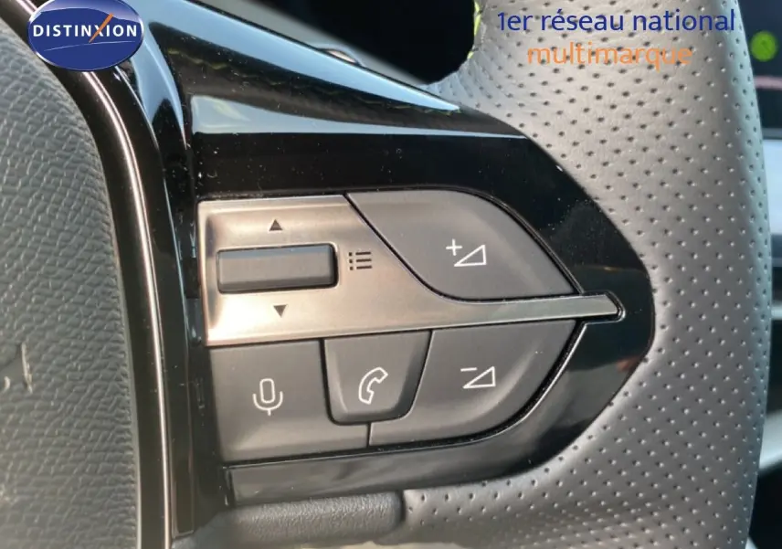Gros plan sur les commandes multifonctions à gauche du volant perforé d’une Peugeot 308 Hybrid blanche.