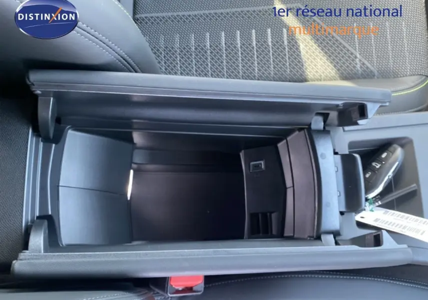Vue plongeante sur le rangement central ouvert de la Peugeot 308 Hybrid blanche, avec intérieur tissu noir et coutures vertes.