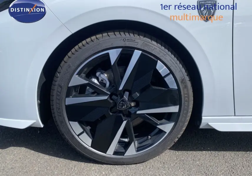 Gros plan sur la roue avant droite d'une Peugeot 308 Hybrid blanche, mettant en valeur la jante noire et argentée au design moderne.