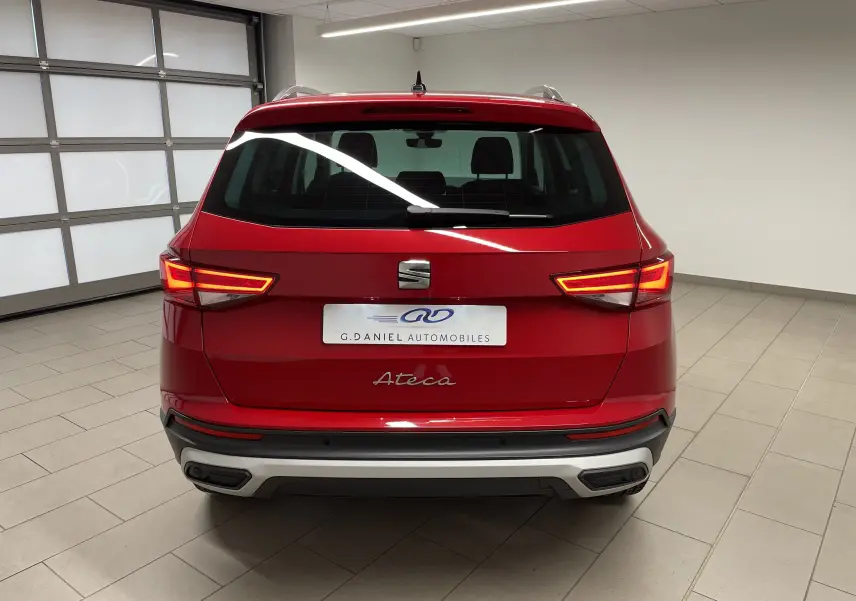 Vue arrière du SUV SEAT Ateca 2024 en Rouge Velvet métallisé avec feux allumés dans un garage intérieur.