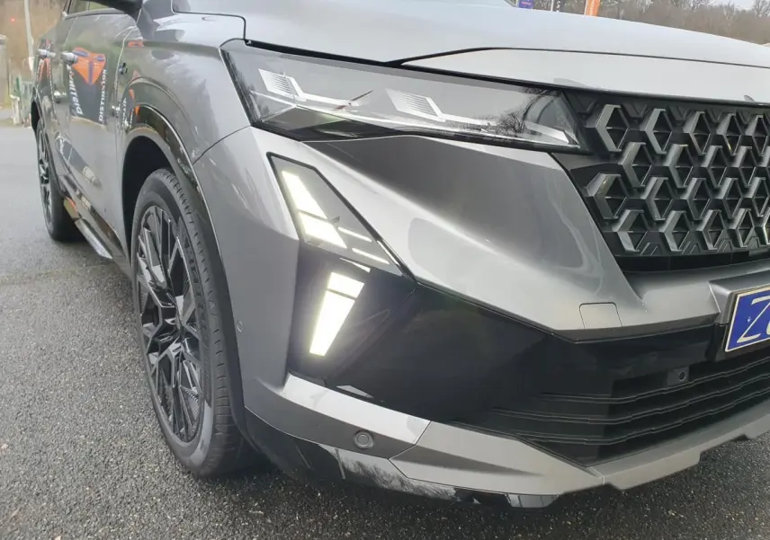 Gros plan sur l'avant droit du Renault Austral gris schiste avec calandre noire et feux LED allumés.