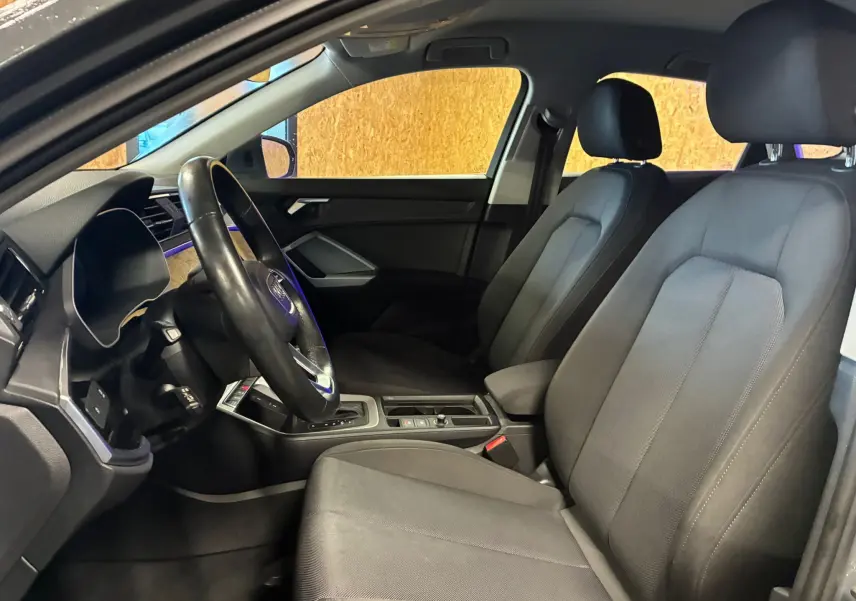 Vue intérieure côté conducteur de l'Audi Q3 Sportback 2021 avec sièges noirs et volant multifonctions cuir.