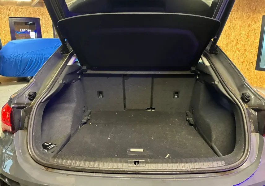 Coffre ouvert vu de l'arrière d'un Audi Q3 Sportback gris, montrant l'espace de chargement vide et les finitions intérieures.