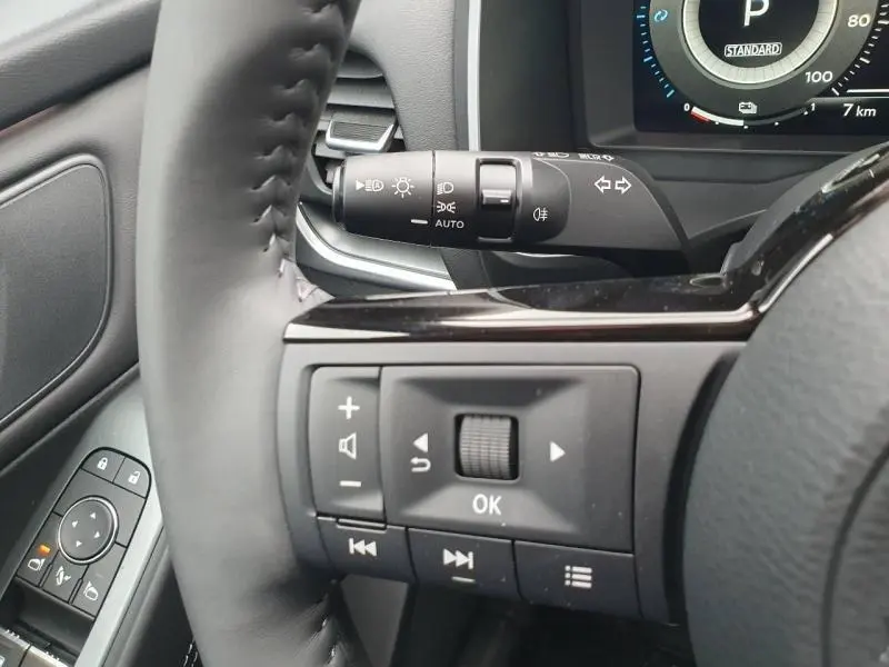 Gros plan sur le volant cuir noir et commandes multifonctions du Nissan Qashqai Hybrid e-POWER gris Squale, tableau de bord partiel visible.