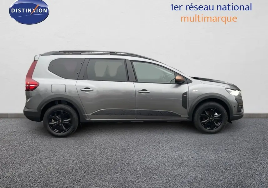 Vue de profil côté droit d'un Dacia Jogger gris schiste métal, avec jantes noires et toit équipé de barres de toit.