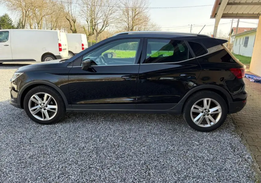 Vue de profil côté gauche d’un SEAT Arona noir 2020 garé sur un sol gravillonné avec jantes alliage visibles.