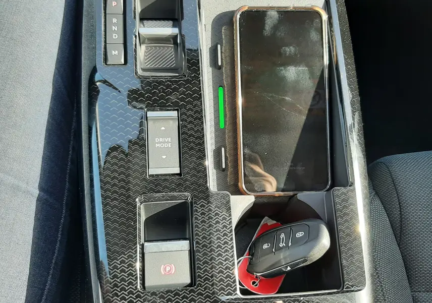 Vue plongeante sur la console centrale noire brillante du Citroën C5 Aircross hybride, avec clé et smartphone posés.