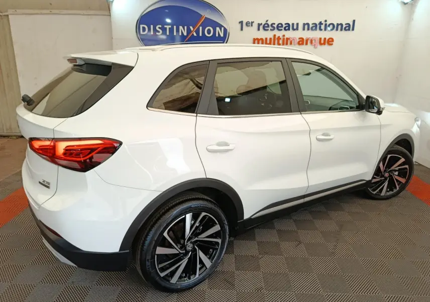 Vue 3/4 arrière droite du MG ZS blanc 2026 avec jantes noires et feux arrière LED allumés dans un showroom.
