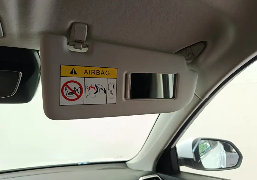 Vue intérieure côté conducteur du pare-soleil beige avec miroir et avertissement airbag dans un MG ZS blanc hybride.
