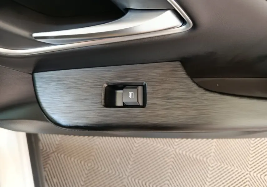 Gros plan sur la commande de lève-vitre intégrée dans la porte intérieure noire du MG ZS blanc.
