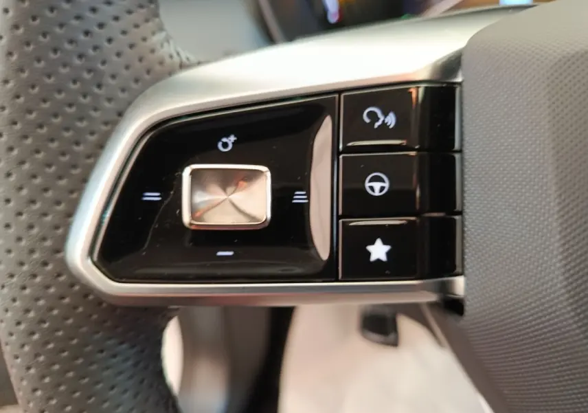 Gros plan sur les commandes noires et argentées du volant perforé côté gauche du MG ZS blanc hybride 2026.