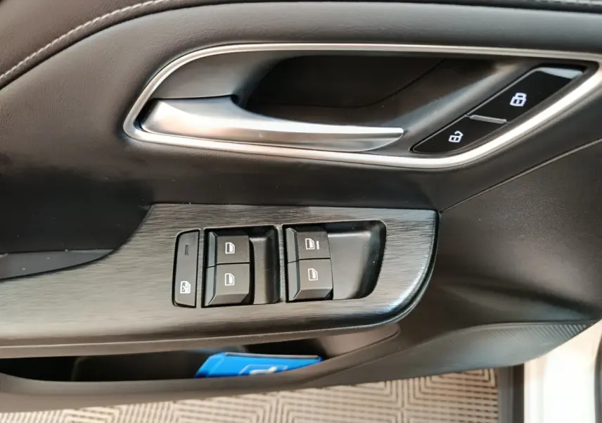Gros plan sur la porte côté conducteur du MG ZS blanc, montrant les commandes de vitres et la poignée intérieure argentée.