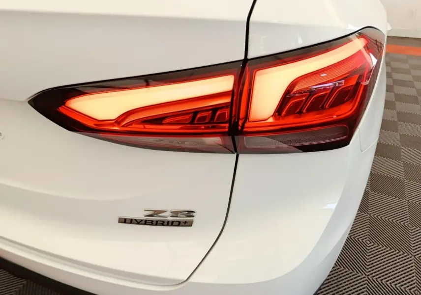 Gros plan sur le feu arrière droit et le logo Hybrid+ du MG ZS blanc, vue arrière côté droit.