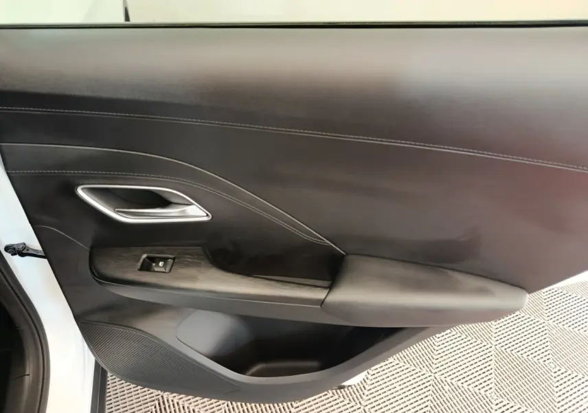 Vue intérieure côté gauche de la porte avant blanche du MG ZS 1.5L Hybrid+ Luxury avec accoudoir et commande de fenêtre.