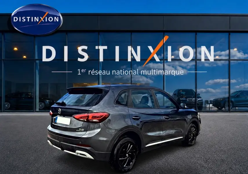 Vue 3/4 arrière droite du MG ZS 1.5 hybrid Camden grey, avec feux arrière LED et jantes noires devant un showroom Distinxion.