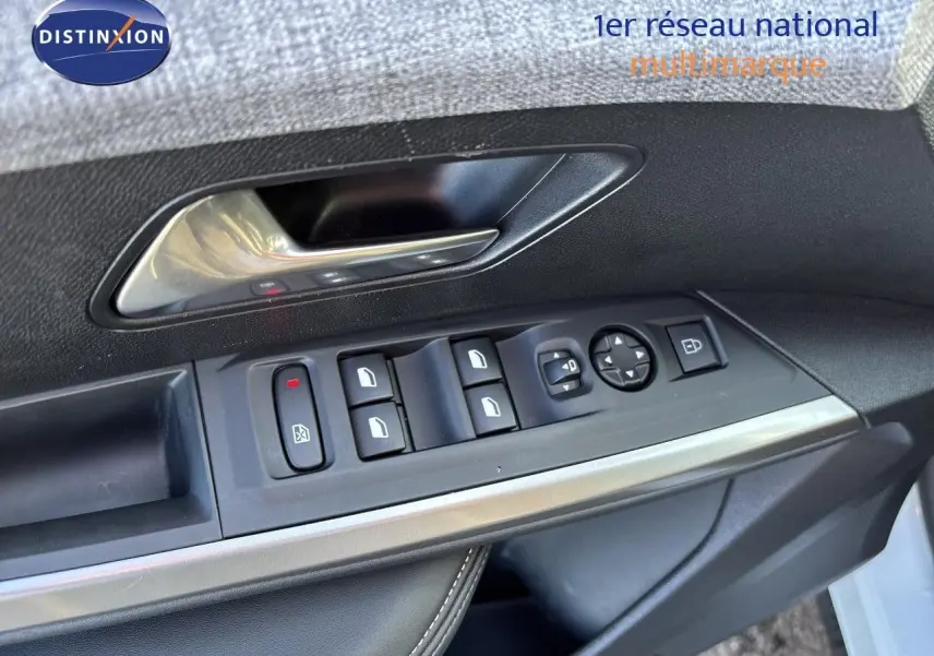 Gros plan sur la commande des vitres et rétroviseurs côté gauche d’une Peugeot 5008 blanche, avec poignée intérieure argentée.