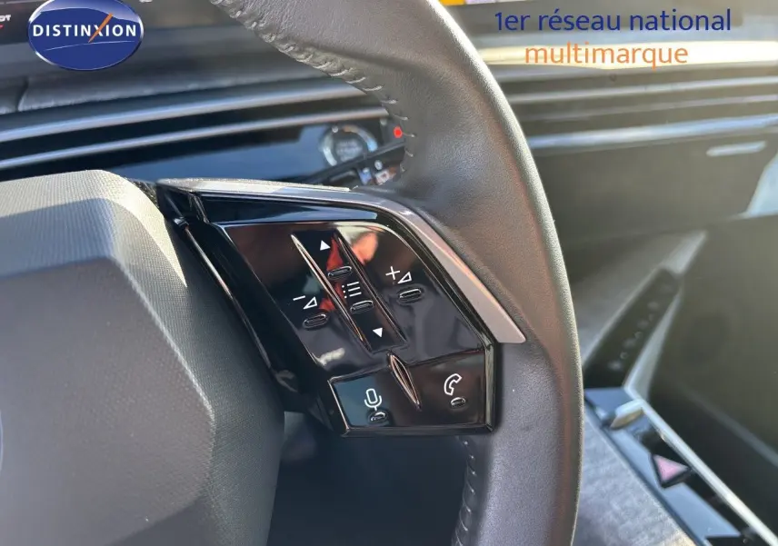 Gros plan sur les commandes multifonctions noires du volant côté gauche du Peugeot 5008 blanc Okenite, intérieur moderne.