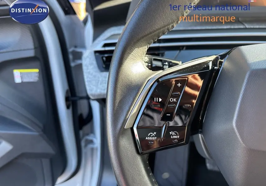 Vue rapprochée du volant noir du Peugeot 5008 blanc Okenite 2025, avec commandes multifonctions visibles côté gauche.