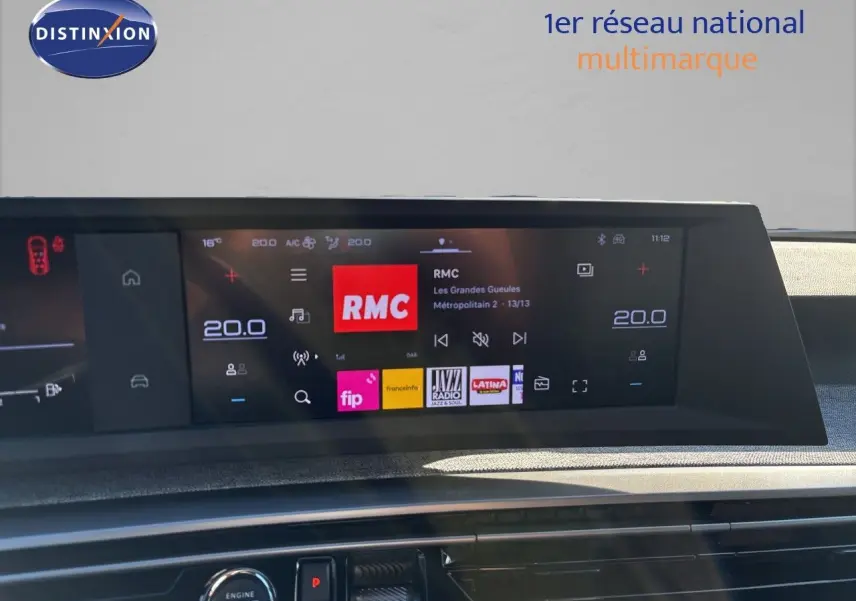 Écran tactile central du tableau de bord du Peugeot 5008 hybride 2025 affichant la radio RMC et la climatisation à 20°C.