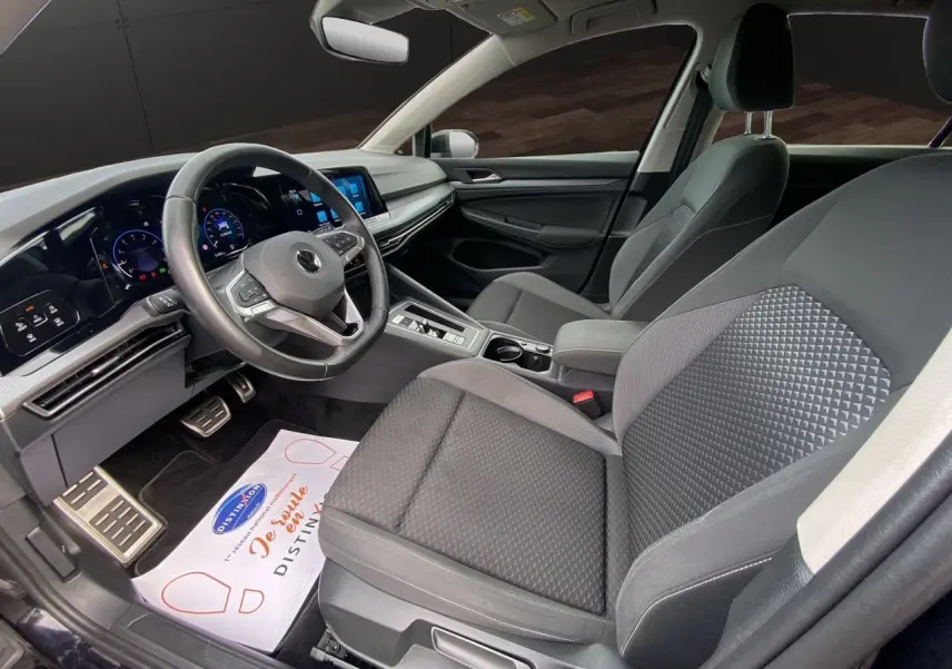 Intérieur noir de la Volkswagen Golf VIII vue côté conducteur, avec tableau de bord numérique et sièges tissu gris foncé.