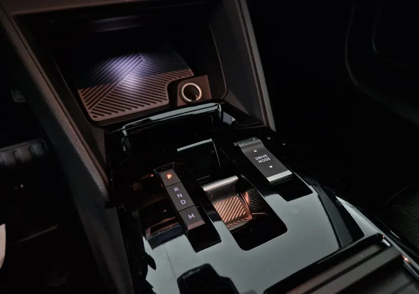 Gros plan sur la console centrale noire brillante de la Citroën C4 1.2 Hybrid 2025 avec sélecteur de boîte auto et bouton Drive Mode.
