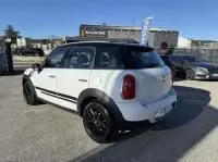 Vue 3/4 arrière droite d'une MINI Countryman Cooper 122 Pack Chili blanche avec toit noir et jantes noires, en extérieur.