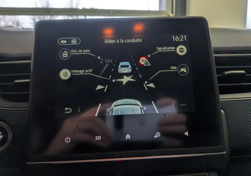 Écran tactile intérieur montrant l’aide à la conduite du Renault Arkana TCe 140 gris métal, avec alertes de distance et signalisation.