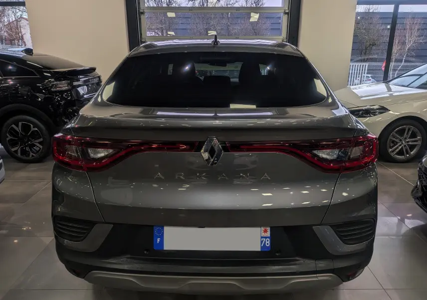 Vue arrière d'un Renault Arkana gris métal 2022 dans un showroom, avec feux arrière allongés et logo central lumineux.