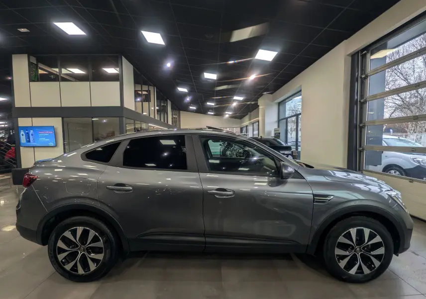 Vue de profil côté gauche d'un Renault Arkana gris métal 2022 en hybride essence, avec jantes bi-ton et vitres teintées.