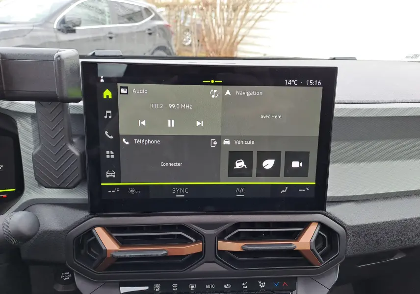 Vue intérieure centrée sur l'écran tactile et les aérateurs cuivrés du tableau de bord du Dacia Bigster noir nacré.