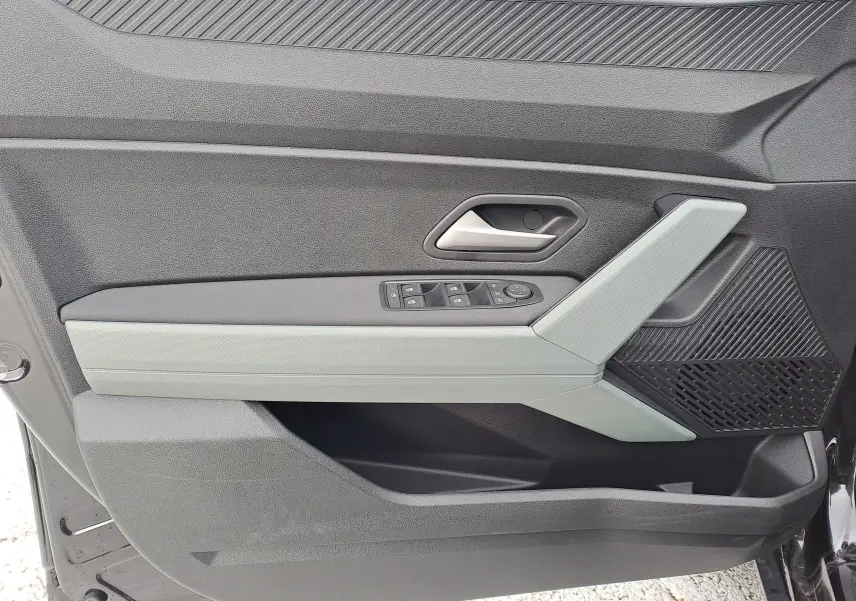 Vue intérieure côté gauche de la porte avant noire nacrée du Dacia Bigster avec accoudoir gris clair et commandes de vitres.