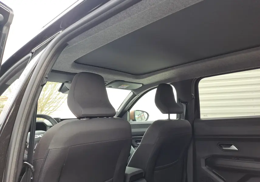 Vue intérieure arrière montrant les sièges avant en tissu gris et le toit noir nacré du Dacia Bigster 2025.